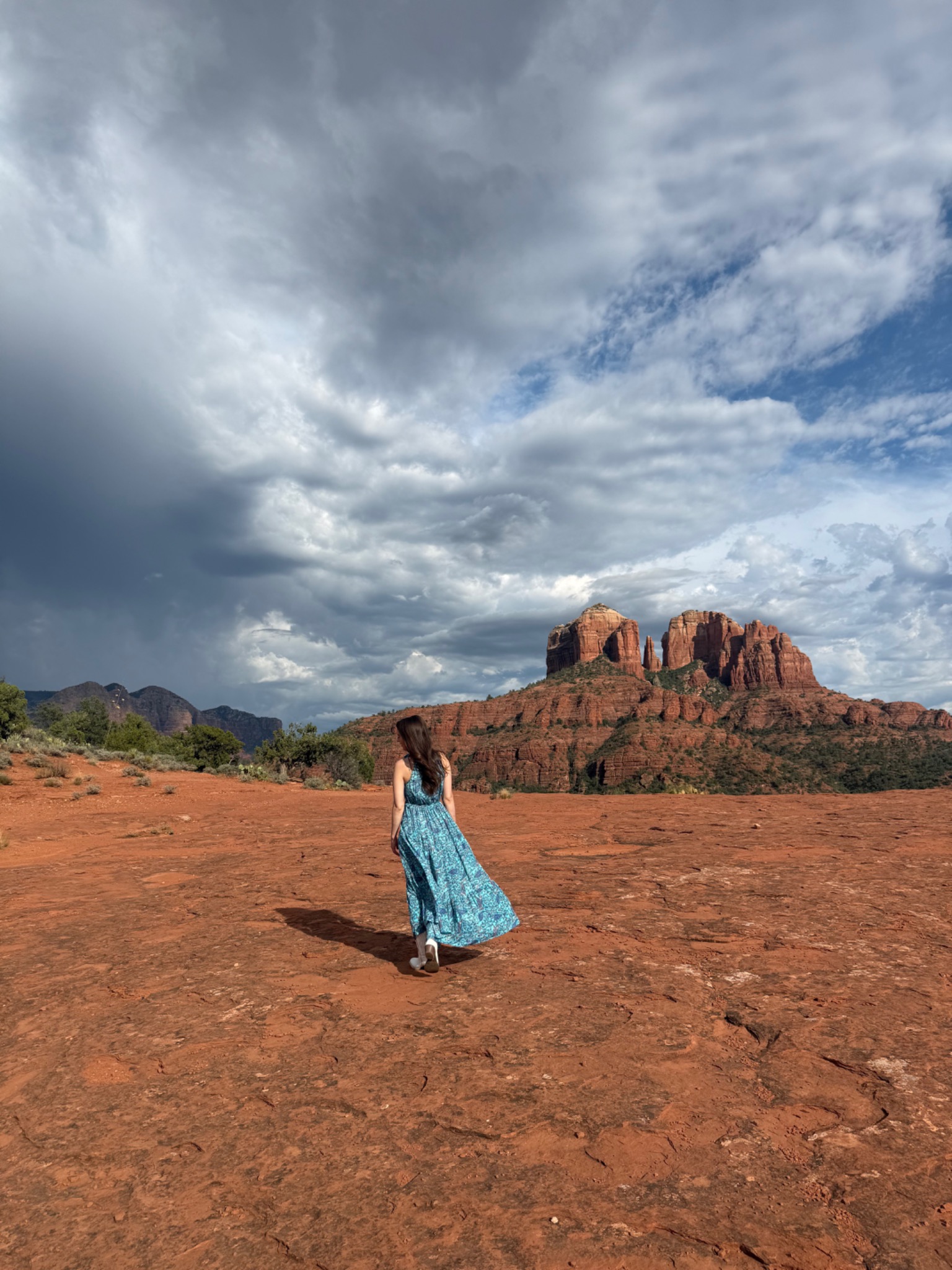 Jacquelyn in a blue dress with Cathedral Rock and a dramatic Sedona sky