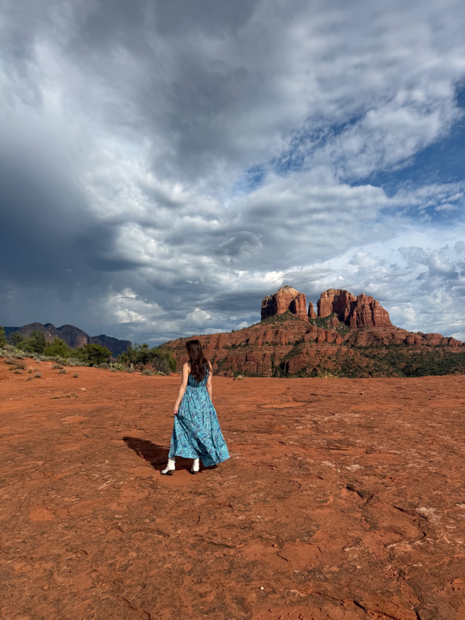 Jacquelyn walking across the Sedona red rocks beneath a dramatic sky
